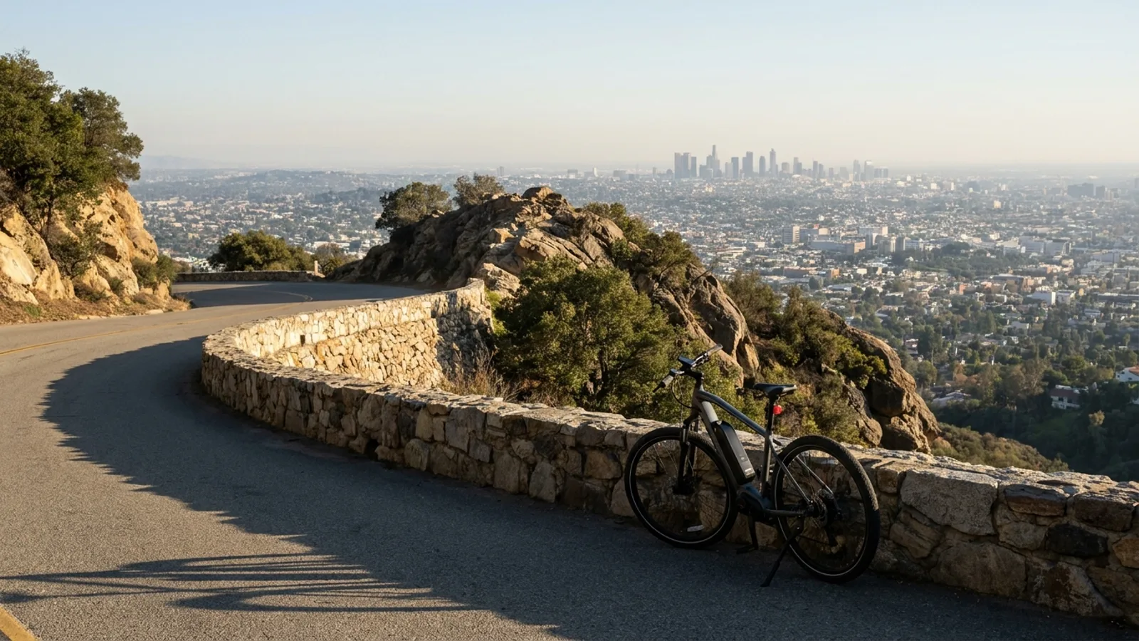 Electric bike at a stone wall on a paved loop road along a wooded rocky ridge with a wide view east across a hazy plain toward a distant skyline