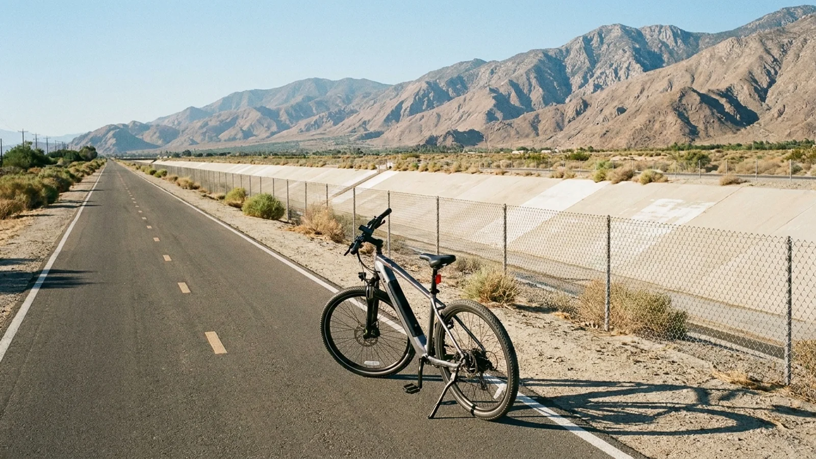 Electric bike on a long straight paved path beside a wide concrete flood control channel running toward dry mountains