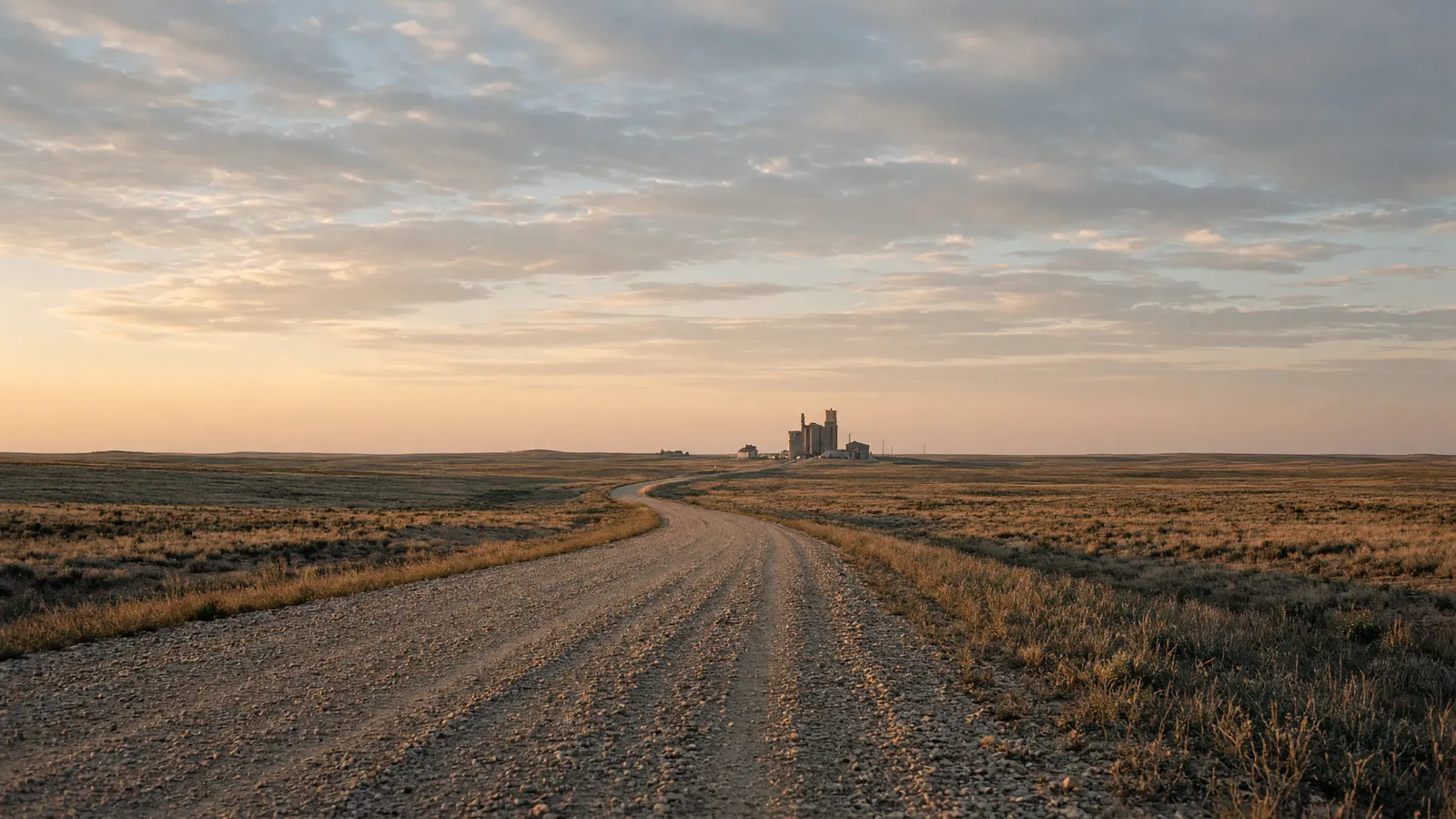 Empty High Plains packed gravel road through shortgrass toward a grain elevator, Cheyenne County, Nebraska