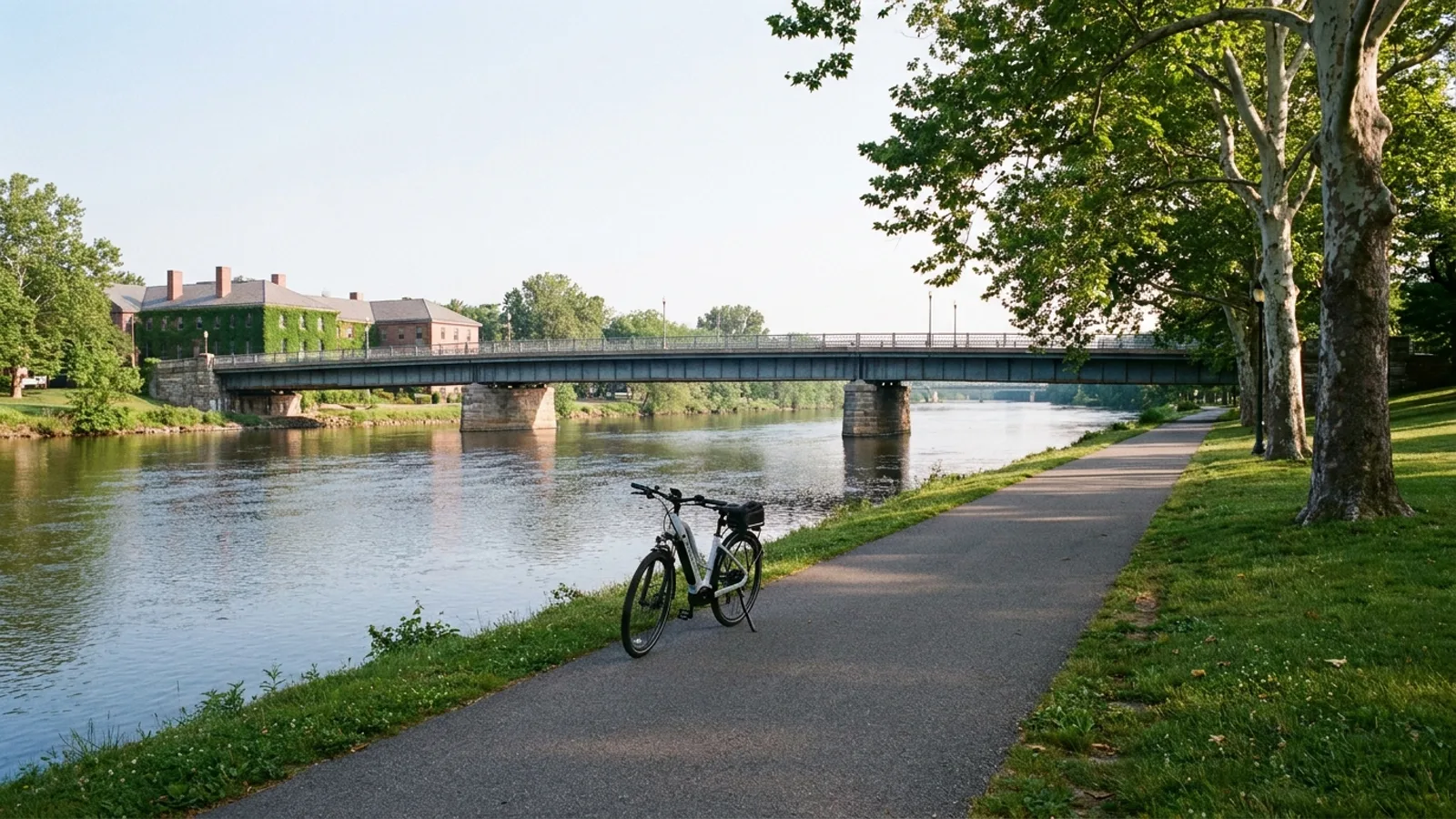 Electric bike on a paved riverside park path beside a wide slow river with bridges crossing, in a New Jersey college town