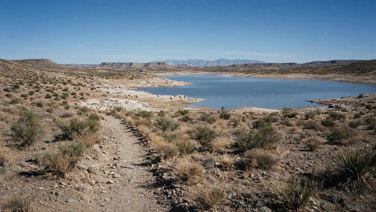 Empty Elephant Butte Lake shoreline path through desert scrub toward a blue reservoir, Sierra County, New Mexico