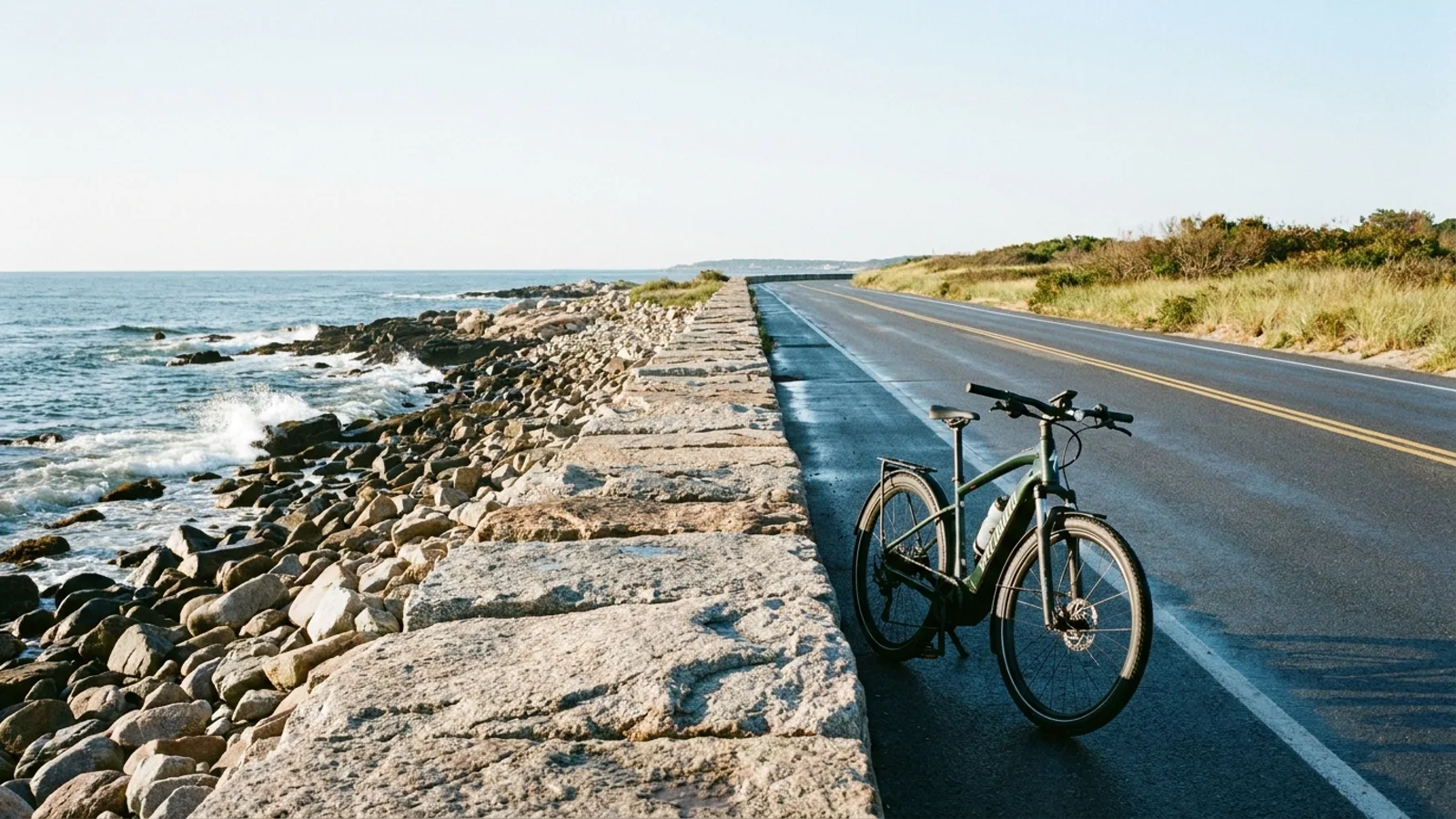 Electric bike parked at a low granite seawall beside a two-lane coastal boulevard above a rocky Atlantic shore with open ocean beyond