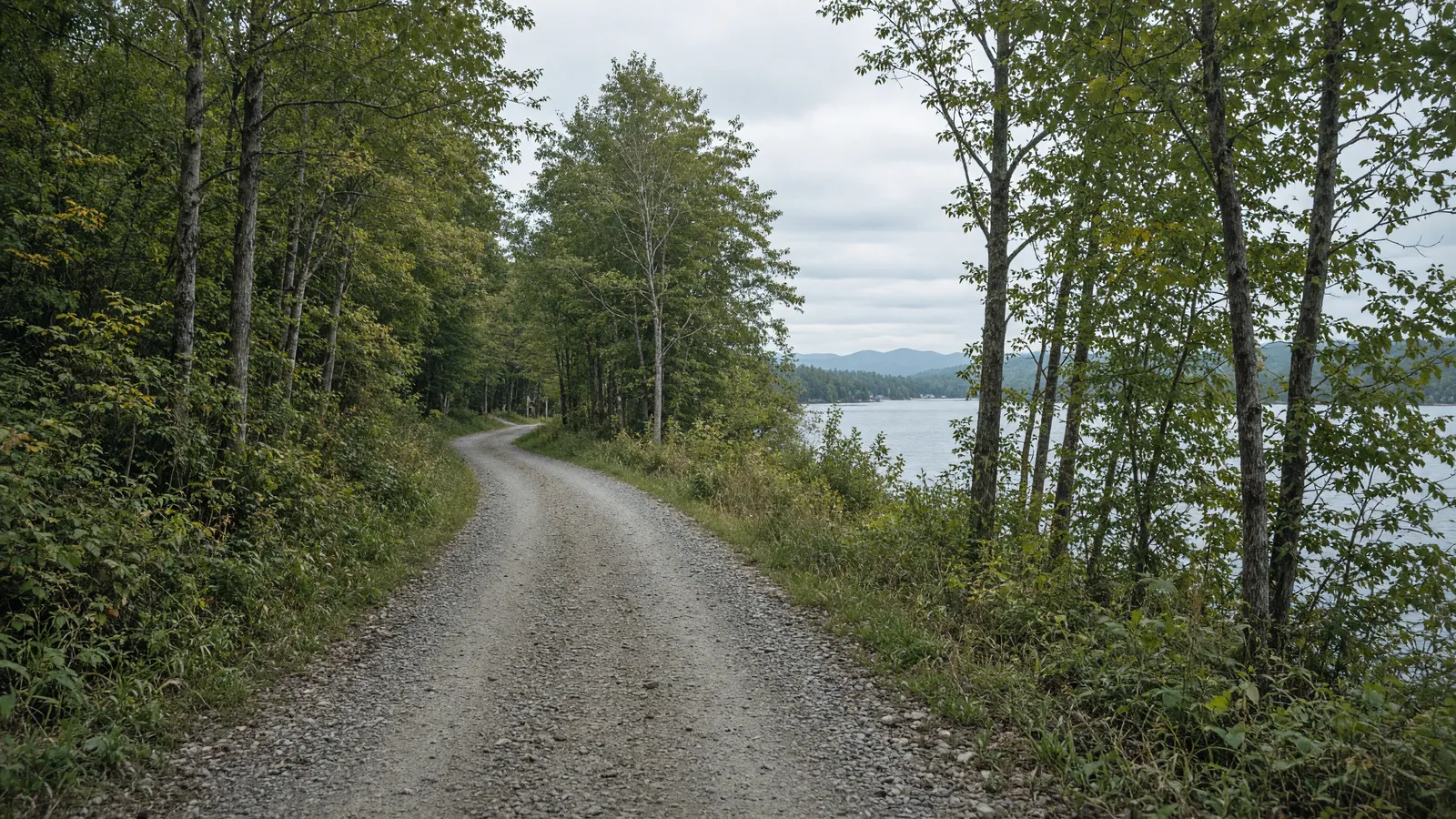Empty gravel rail-trail corridor toward a northern lake shore in Orleans County, Vermont