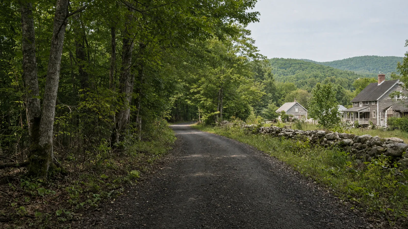 Empty mixed-surface rail-trail corridor through forest and village edge in Rutland County, Vermont