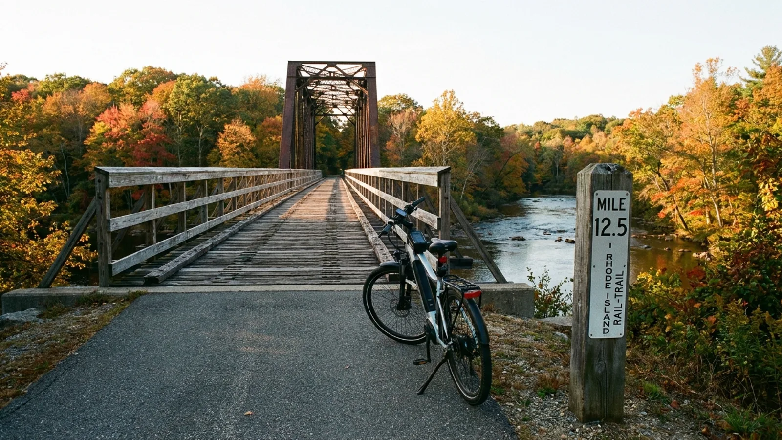 Electric bike on a paved rail-trail approaching a restored steel trestle bridge over a river in Rhode Island